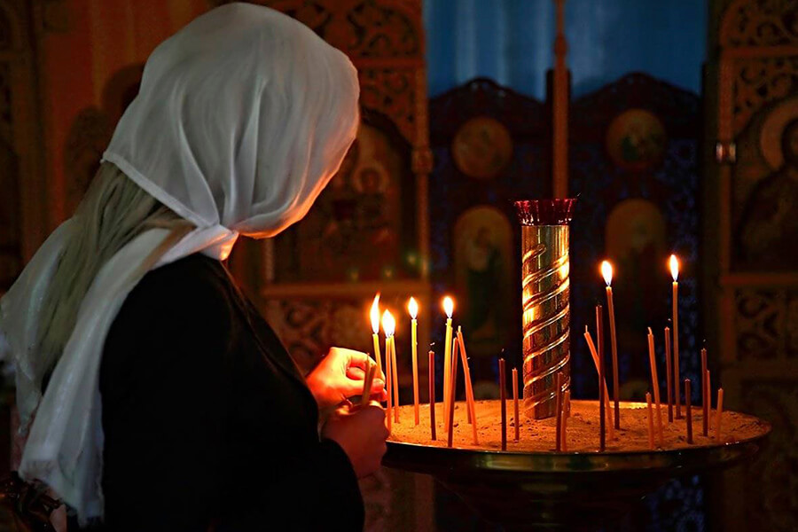 женщина ставит свечу в храме